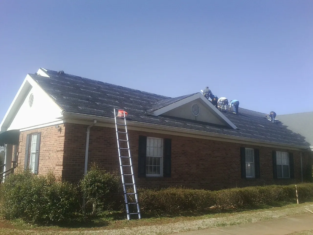 Crew tearing shingles off a brick ranch roof with a ladder set — Emergency Roof Repair work by our crew in Thousand Oaks