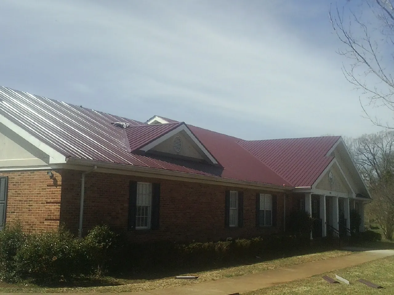 Red metal roof with gabled entries on a long brick building, from a Hail Damage Roof Repair job in Thousand Oaks