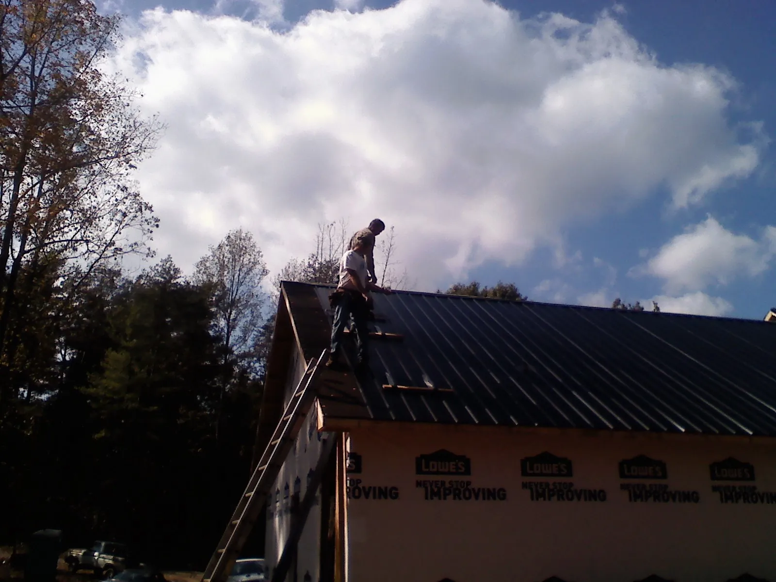 Roofer fastening dark metal panels high against a cloudy sky, from a Roof Inspection job in Thousand Oaks